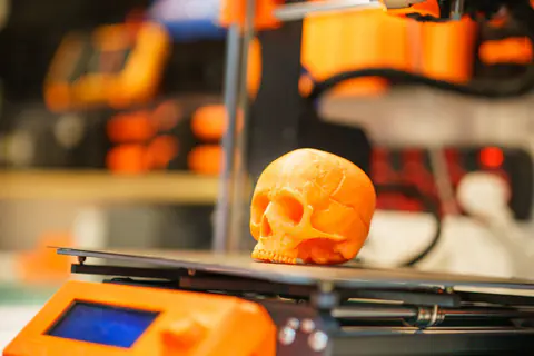 Orange 3D-printed skull model on a 3D printer in a workshop
